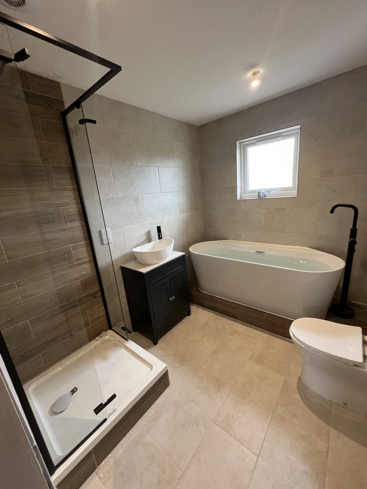 Bathroom with freestanding bath, stone-effect tiles and black shower frame